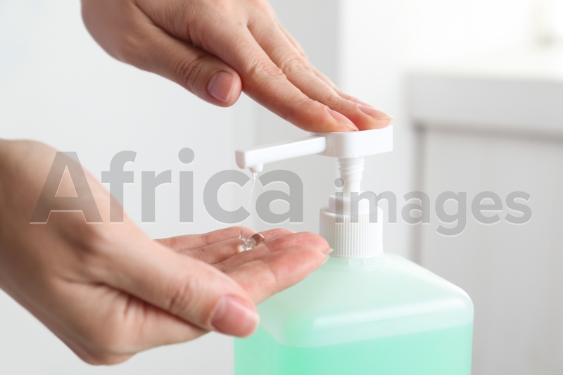 Woman applying antiseptic gel on hand indoors, closeup