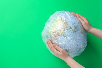 Photo of Woman holding globe packed in bubble wrap and space for text on light green background, top view. Environmental conservation