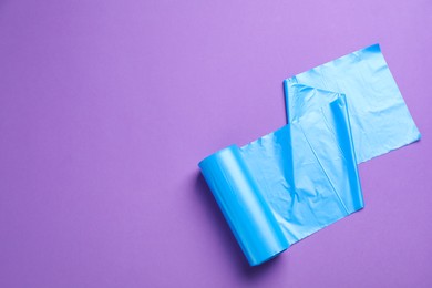 Roll of light blue garbage bags on violet background, top view. Space for text