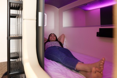 Photo of Happy young woman lying in capsule of pod hostel