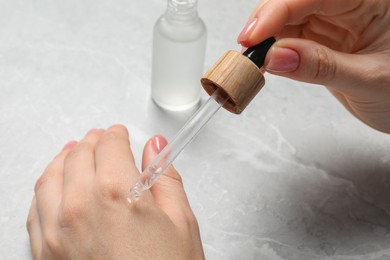 Woman dripping serum from pipette on her hand at light grey marble table, closeup