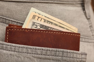 Wallet with dollar banknotes in pocket of grey jeans, closeup. Spending money