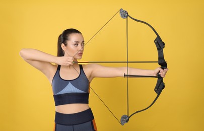 Sporty young woman practicing archery on yellow background