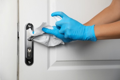 Woman cleaning door handle with antiseptic in office, closeup