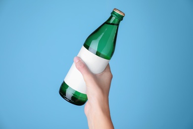Woman holding glass bottle with soda water on light blue background, closeup