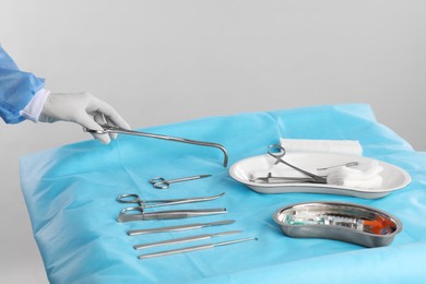 Doctor holding forceps over table with surgical instruments against light background, closeup