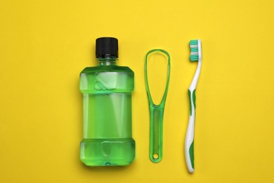 Tongue cleaner, mouthwash and toothbrush on yellow background, flat lay