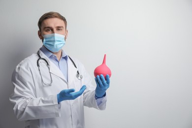 Doctor holding rubber enema on grey background. Space for text