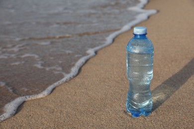 Photo of Plastic bottle of fresh water on wet sand near sea. Space for text