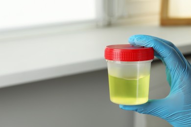 Doctor holding container with urine sample for analysis indoors, closeup. Space for text
