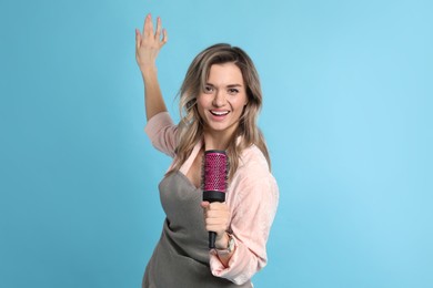 Beautiful young woman singing into hairbrush on light blue background