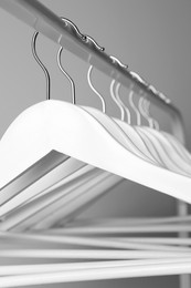 White clothes hangers on metal rail against light background, closeup