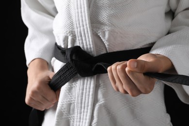 Man in keikogi with black belt on dark background, closeup. Martial arts uniform