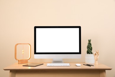 Comfortable workplace with blank computer display on desk and plant near beige wall. Space for text