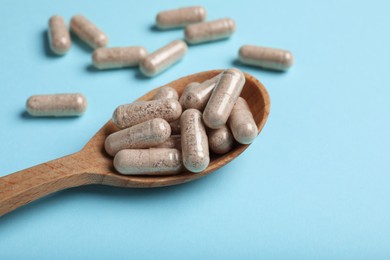 Gelatin capsules in spoon on light blue background