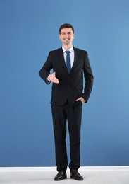 Business trainer reaching out for handshake on color wall background