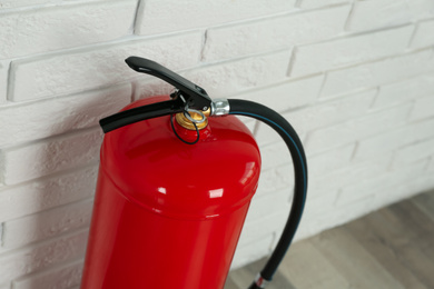 Fire extinguisher near white brick wall indoors, closeup