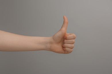 Woman showing thumb up on grey background, closeup