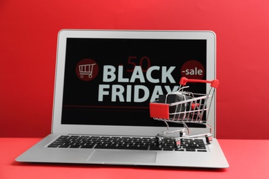 Laptop with Black Friday announcement, small shopping cart and gift on red background
