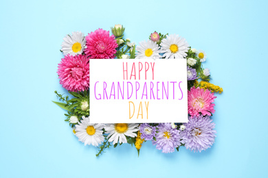 Flat lay composition with beautiful aster flowers and phrase HAPPY GRANDPARENTS DAY on light blue background