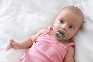 Cute little baby with pacifier lying on bed, top view