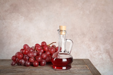 Glass jug with wine vinegar and fresh grapes on wooden table against color background