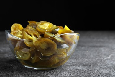 Photo of Glass bowl with slices of pickled green jalapeno peppers on grey table, space for text