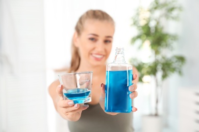 Woman holding bottle and glass with mouthwash in bathroom. Teeth care