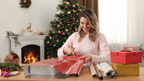 Photo of Beautiful young woman wrapping Christmas gift at home