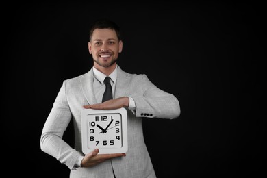 Happy businessman holding clock on black background, space for text. Time management