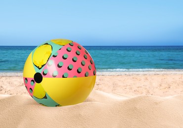 Colorful beach ball on sandy coast near sea, space for text 