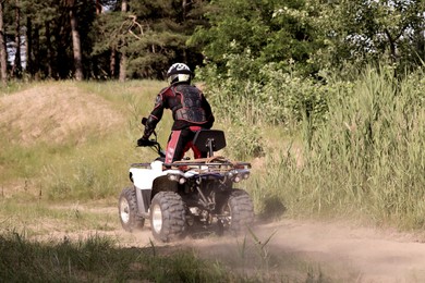 Photo of Man driving modern quad bike on sandy road, back view. Extreme sport