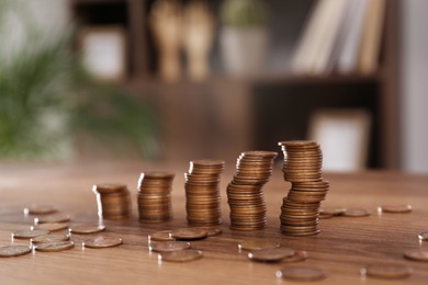 Stacks of coins on wooden table against blurred background