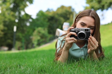 Young woman with camera taking photo on green grass outdoors, space for text. Interesting hobby