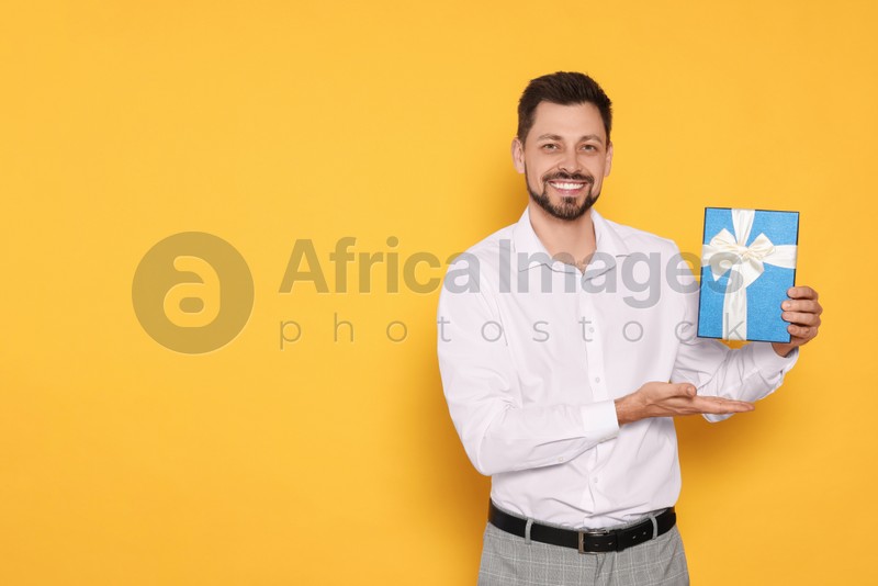 Happy man with gift box on yellow background, space for text