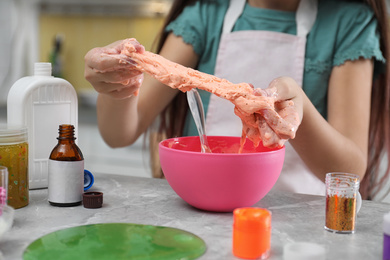 Little girl kneading DIY slime toy at table indoors, closeup