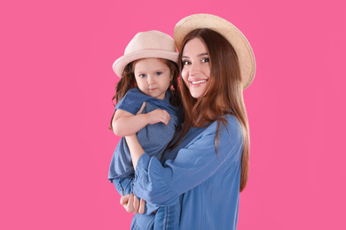 Young mother and little daughter with hats on pink background