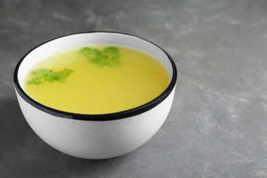 Photo of Delicious chicken bouillon with parsley on grey table. Space for text