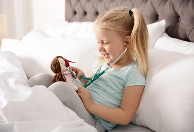 Cute child imagining herself as doctor while playing with stethoscope and doll at home