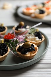 Photo of Delicious tartlets with caviar and cream cheese served on white wooden table, closeup