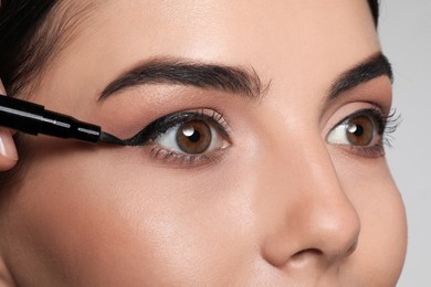 Photo of Artist applying black eyeliner onto woman's face on grey background, closeup