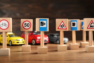 Photo of Many different miniature road signs and cars on wooden table. Driving school