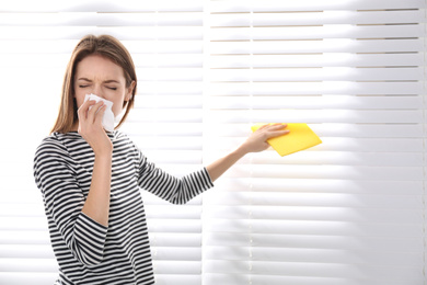Young woman suffering from dust allergy while cleaning window blinds at home