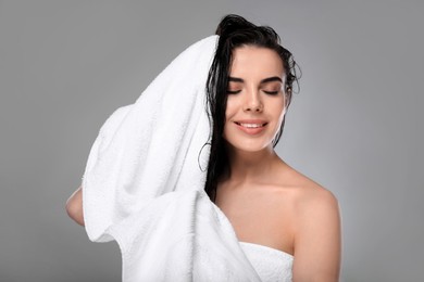 Happy young woman drying hair with towel after washing on light grey background