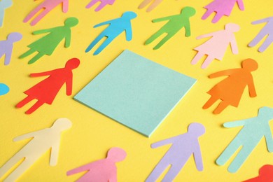 Photo of Many different paper human figures around blank card on yellow background, space for text. Diversity and inclusion concept
