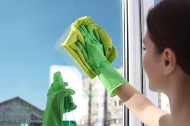 Young woman cleaning window glass with rag and detergent at home, closeup
