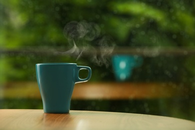 Cup of hot drink on wooden table against blurred background, space for text