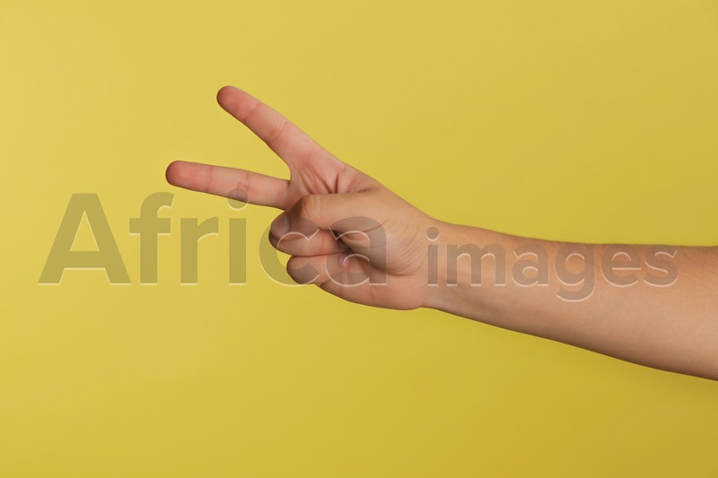Photo of Teenage boy showing two fingers on yellow background, closeup