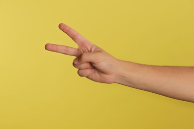 Teenage boy showing two fingers on yellow background, closeup