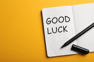 Image of Open notebook with GOOD LUCK on orange background, top view. Space for text